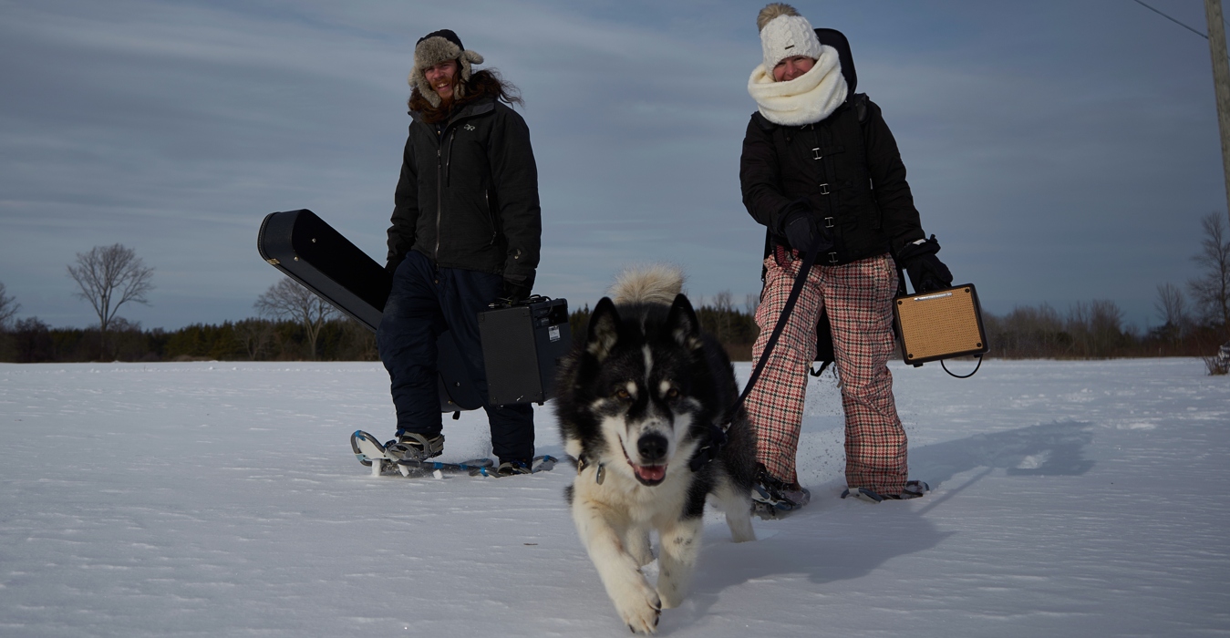 Jenn and Matt with their gear and husky in a snowy field