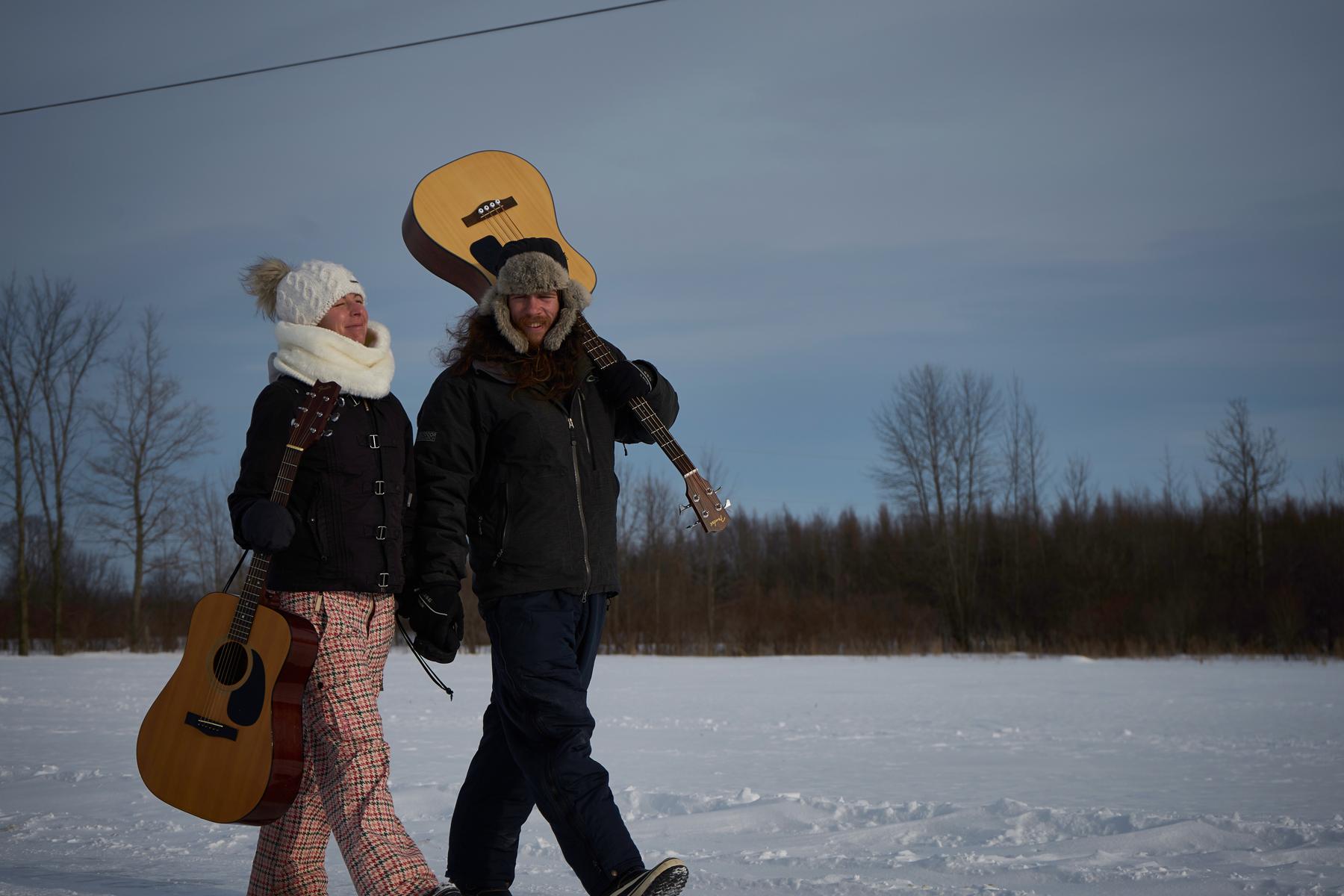 Jenn and Matt holding hands in snowy field with instruments