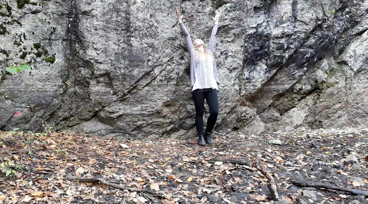 Jenn with arms up at the bottom of a small cliff
