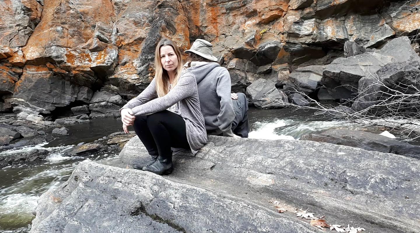 Jenn and Matt back to back on rock beside creek