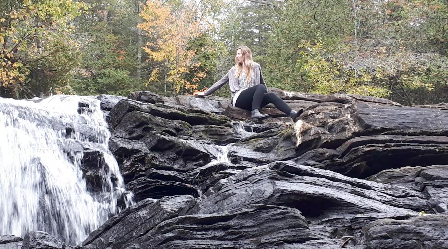 Jenn sitting on rocks beside small waterfall